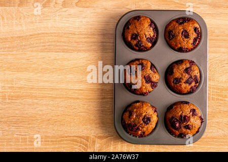 Blick von oben auf die sechs Banane - Kirsch Muffins auf einem Tablett mit hellbraunem Hintergrund, flach. Stockfoto