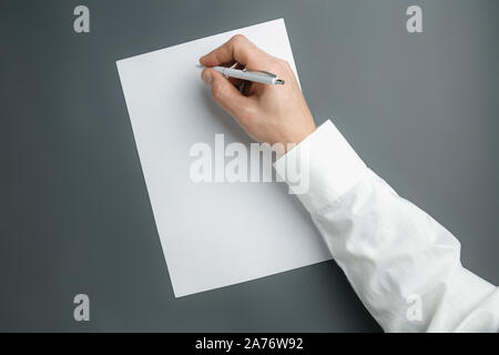 Männliche Hand mit Stift und schreiben auf leeres Blatt auf grauem Hintergrund für Text oder Design. Leere Vorlagen für Kontakt, Werbung oder für den Einsatz in Unternehmen. Finanzen, Büro, Einkäufe. Mock up. Copyspace. Stockfoto
