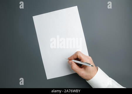 Männliche Hand mit Stift und schreiben auf leeres Blatt auf grauem Hintergrund für Text oder Design. Leere Vorlagen für Kontakt, Werbung oder für den Einsatz in Unternehmen. Finanzen, Büro, Einkäufe. Mock up. Copyspace. Stockfoto