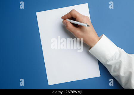 Männliche Hand mit Stift und schreiben auf leeres Blatt auf blauem Hintergrund für Text oder Design. Leere Vorlagen für Kontakt, Werbung oder für den Einsatz in Unternehmen. Finanzen, Büro, Einkäufe. Mock up. Copyspace. Stockfoto