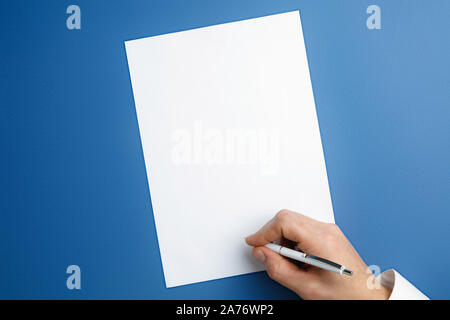 Männliche Hand mit Stift und schreiben auf leeres Blatt auf blauem Hintergrund für Text oder Design. Leere Vorlagen für Kontakt, Werbung oder für den Einsatz in Unternehmen. Finanzen, Büro, Einkäufe. Mock up. Copyspace. Stockfoto