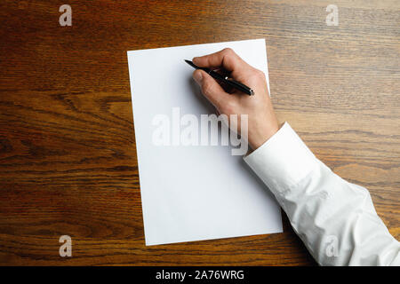 Männliche Hand mit Stift und schreiben auf leeres Blatt auf hölzernen Hintergrund für Text oder Design. Leere Vorlagen für Kontakt, Werbung oder für den Einsatz in Unternehmen. Finanzen, Büro, Einkäufe. Mock up. Copyspace. Stockfoto