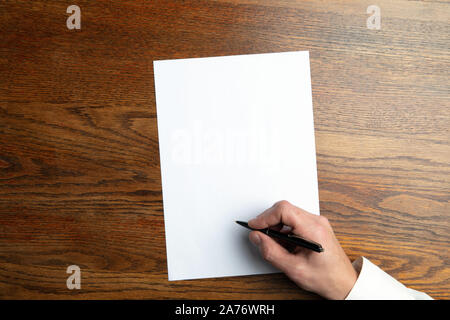 Männliche Hand mit Stift und schreiben auf leeres Blatt auf hölzernen Hintergrund für Text oder Design. Leere Vorlagen für Kontakt, Werbung oder für den Einsatz in Unternehmen. Finanzen, Büro, Einkäufe. Mock up. Copyspace. Stockfoto