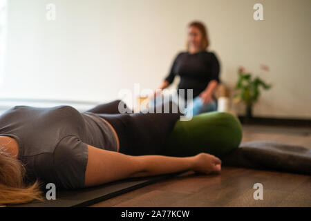 Selektiver Fokus Foto einer erwachsenen Frau sitzt auf einem Yoga Matte mit einer Kamera auf einem Stativ, Videoaufnahmen Stockfoto