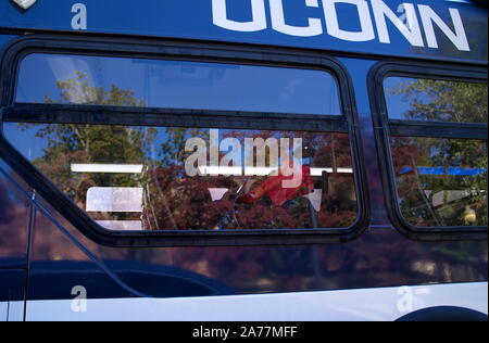 Storrs, CT USA. Okt 4 2019. Studentin am Telefon beim Reiten shuttle bus mit falllaub Farben auf Fenster, Stockfoto