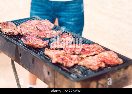 BBQ Beef Steak auf dem Grill rauchen über glühende Kohlen. Mann kochen Grill draußen. Nahaufnahme der leckere Rindersteaks gebraten auf Grill. Organisches Fleisch gebraten auf rustikalen Holzkohle Grill. Stockfoto