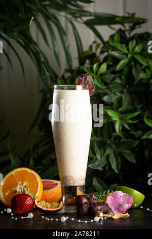 Milchshake mit ein Datum in ein Glas und Früchte auf einem Hintergrund von grünen Blättern Stockfoto