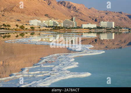 Reflexion der Berge, Hotels und Palmen im Wasser des Toten Meeres mit Salz Formationen. Israel Stockfoto