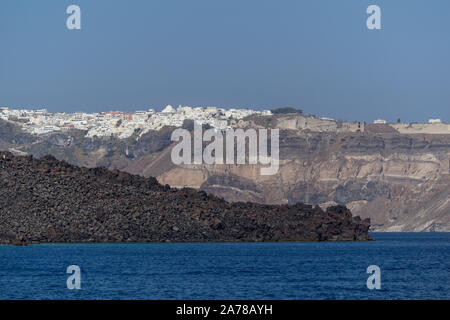 Ein langer Blick auf Santorini schwarz erstarrter Lava in das Meer Krater mit Fira im Hintergrund Stockfoto