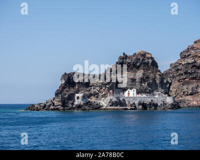 Blick vom Meer der Lava Rock Isle of St Nicholas Oia Santorini Griechenland ruhiges Wasser klare blaue Himmel Stockfoto