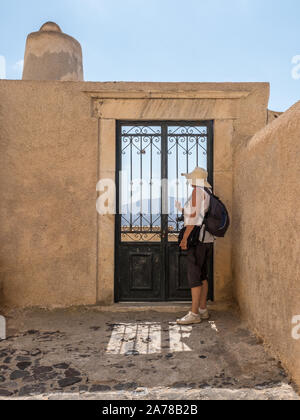 Eine Frau, die Touristen in der Sonne hat sie den Blick durch die schmiedeeisernen Tor mit Blick auf die Berge Fira Santorini Stockfoto