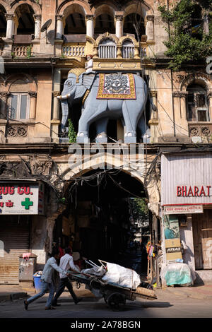 Zwei Männer push Trolley Vergangenheit der legendären Elefantentor in Kalbadevi Road, Mumbai, Indien, ein Gebäude, das einst ein Gujarati Sprache Theater untergebracht Stockfoto