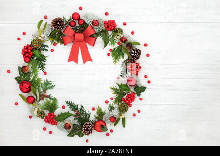 Christmas wreath Dekoration mit einem roten glittter Bogen, Christbaumkugeln, lose Stechpalme Beeren und Winter Flora auf rustikalem Holz Hintergrund mit Kopie Raum, Stockfoto