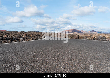 Low Angle View von leeren Asphalt Straße Straße durch Dürren vulkanische Landschaft gegen den blauen Himmel Stockfoto