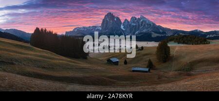 Luftige Herbstsonnenaufgangsszenerie mit gelben Lärchen und kleinem Alpenbau und Geisler-Berggruppe im Hintergrund. Seiser Alm (Seiser Alm Stockfoto