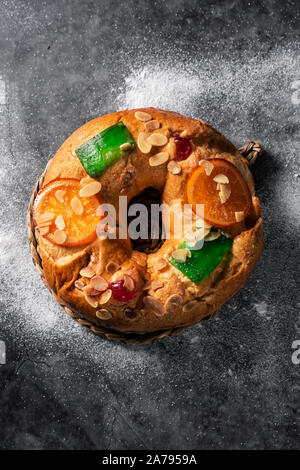 Hohe Betrachtungswinkel eines roscon de Reyes, drei Könige Kuchen auf epiphanie Tag gegessen Spanisch, auf einem grauen rustikalen Tisch mit Puderzucker bestreut Stockfoto