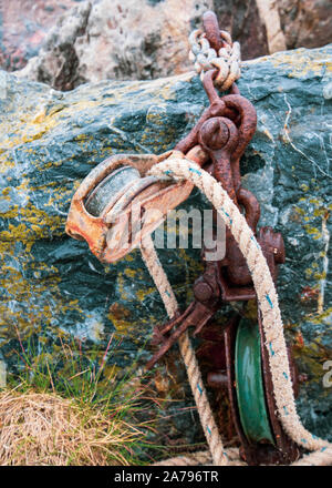 Rostige Kette auf Green Rock mit Riemenscheibe und weißen Seil. Stockfoto