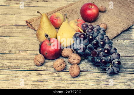 Köstliches Herbst Ernte - auf Sackleinen, einem hölzernen Hintergrund voller Reife Birnen, Äpfel, Trauben und Walnüssen Stockfoto