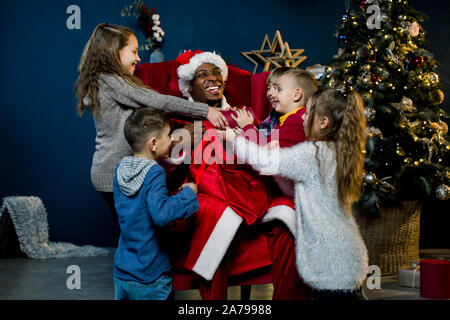 Fünf Kinder in die Tasche der Afrikanischen Santa Claus schauen und Lachen, afrikanische Santa Claus sitzt und gibt präsentiert schöne kleine Kinder in Stockfoto