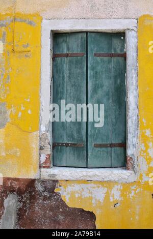 Grünen Fensterläden ein gelbes Haus mit abblätternder Farbe Stockfoto