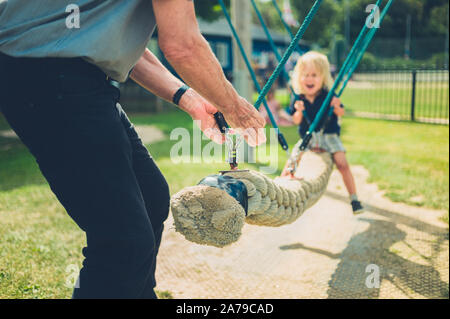 Ein kleines Kind wird auf einer Schaukel von seinem Großvater geschoben Stockfoto