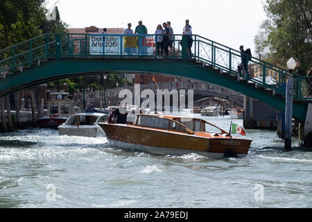 Strahlend, glänzend Wassertaxi auf dem Canal Grande unter einem grünen Fußgängerbrücke mit Leute zu beobachten, eine weitere Brücke im Hintergrund. Stockfoto