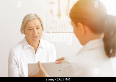 Ältere Frau mit ihrem Arzt für Geriatrie zeigen ihr das Labor die Ergebnisse der neuesten Tests auf einem Tablet-PC. Stockfoto