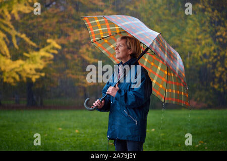 Eine Dame mittleren Alters genießen im Herbst regnerischen Tag im Park Stockfoto
