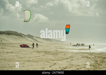 Kite Surfer mit Drachen aloft, zu Fuß über den Strand zum Meer mit board Surfer im Hintergrund. Stockfoto