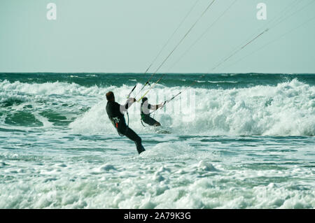 Ein paar Kitesurfer in rauher See durch brechende Wellen in der Nähe des Strandes an der Atlantikküste fahren, Frankreich Stockfoto