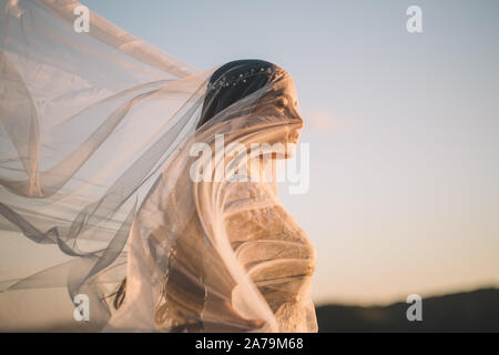 Bildende Kunst, Hochzeit, Glück, Leben, Liebe, Leben. Schöne junge Frau Braut bedeckte ihr Gesicht mit einem Schleier Curling im Wind in der Natur ag Stockfoto