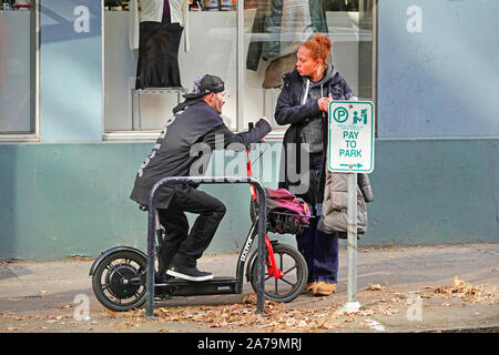 Ein Mann auf einem Roller spricht mit einem Afrikanische amerikanische Frau auf einer Straße in der Innenstadt von Portland, Oregon. Stockfoto