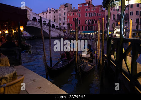 Die Gondolieri und ihre Gondeln vertäut, Warten auf Kunden in den frühen Abend Licht mit künstlichem Licht und die Rialto Brücke im Hintergrund. Stockfoto