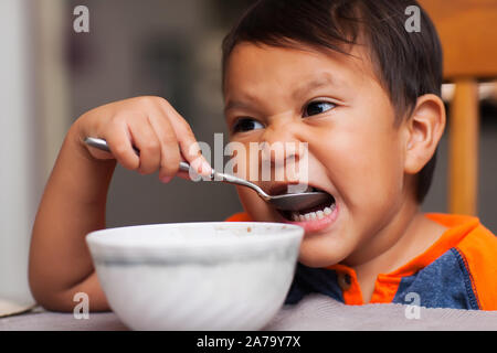 Ein latino Boy einen Bissen von einem Löffel essen und sitzen am Tisch nicht unterstützte zum Frühstück. Stockfoto