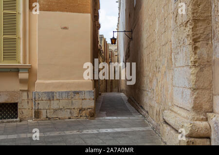 Typische Mdina Straße. Schmale mittelalterliche Straße von Mdina, auch als "stille Stadt" bekannt, gepflastert mit Steinplatten und mit gelben Kalkstein Mauern umgeben, Stockfoto