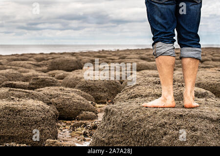 Mann barfuß am Strand von Steinen, der am Ufer des Meeres Stockfoto