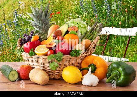 Frühlingswiese mit bunten Blumen und Obst und Gemüse in den Korb und Sitzbank Stockfoto