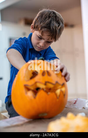 6 Jahre alter Junge, der vor Halloween die Rinde in einem geschnitzten Kürbis herauskratzt, England, Vereinigtes Königreich Stockfoto