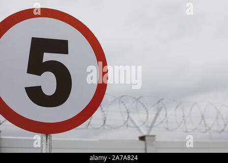 Flache Tiefenschärfe (selektive Fokus) Bild mit einer Höchstgeschwindigkeit Verkehrszeichen vor einer Mauer mit Stacheldraht auf der Oberseite, außerhalb eines staatlichen Insti Stockfoto