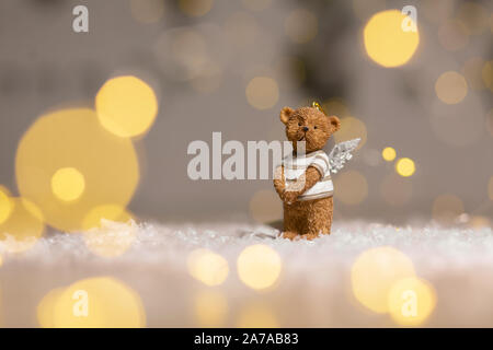 Dekorative Figuren aus einem Thema Weihnachten. Figurine eines süßen Bär mit Angel Wings. Festliches Dekor, warme Bokeh leuchtet. Stockfoto