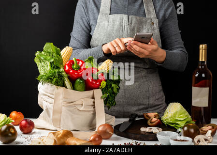 Um essen online. Käufe Konzept. Lebensmittelgeschäft eco Beutel mit Frische, gesunde Lebensmittel und hält eine Frau in den Händen smartphone. Kochen gesund essen. Stockfoto