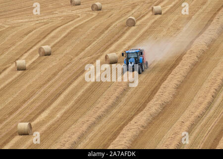 Ein Bauer mit einem blauen Traktor Pressen von Gerste Stroh auf einem Hügel im Feld Aberdeenshire Landschaft Stockfoto