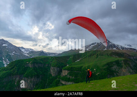 Gudauri, Kazbegi, Georgien: Menschen Paragliding durch den Teufel Tal im Kaukasus. Im Hintergrund die bunten Gipfel von Mount Kazbek Stockfoto