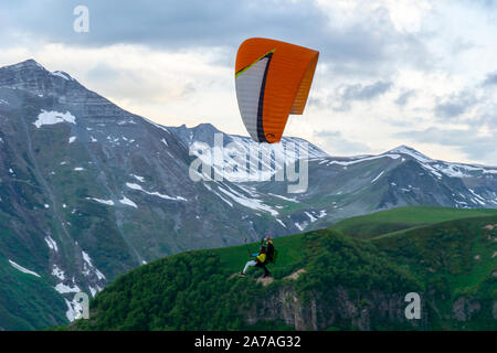 Gudauri, Kazbegi, Georgien: Menschen Paragliding durch den Teufel Tal im Kaukasus. Im Hintergrund die bunten Gipfel von Mount Kazbek Stockfoto