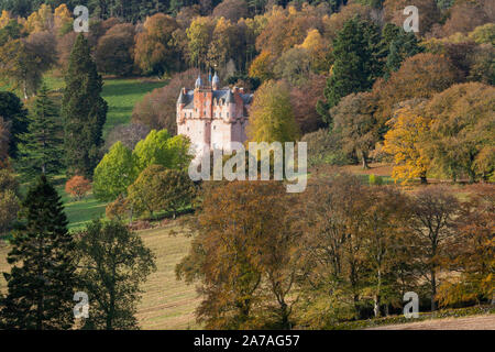 Die rosa Farbe des Craigievar Castle ergänzt die herbstlichen Farben der verschiedenen Bäume auf einem bewaldeten Hang in Aberdeenshire. Stockfoto