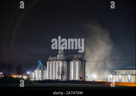 Korn Anlage nachts arbeiten mit Dampf schwimmenden um ihn herum. Die agro farm Metall Lift, hohen Silos mit dunklen Himmel im Hintergrund. Stockfoto