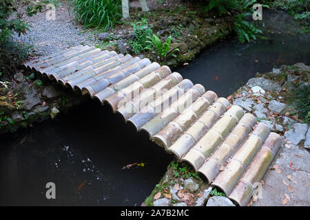 Holzbrücke über einen schmalen Bach im Botanischen Garten in Batumi. Eine Brücke Aus dickem Bambus stammt. Rote Fische schwimmen im Bach. Ein kleiner Teich von Stockfoto