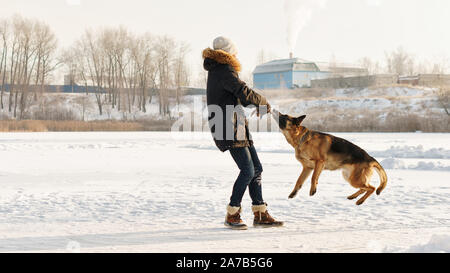 Stilvolle Kerl Spaziergang mit dem Hund. Spaß im Schnee spielen im Freien. Spielerische. Tierliebhaber. Deutscher Schäferhund genießen Sie die Freiheit. Freunde zusammen. Lustige e Stockfoto