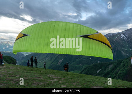 Gudauri, Kazbegi, Georgien: Menschen Paragliding durch den Teufel Tal im Kaukasus. Im Hintergrund die bunten Gipfel von Mount Kazbek Stockfoto