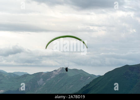 Gudauri, Kazbegi, Georgien: Menschen Paragliding durch den Teufel Tal im Kaukasus. Im Hintergrund die bunten Gipfel von Mount Kazbek Stockfoto